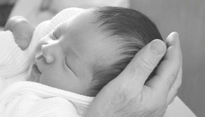A black-and-white image of a newborn baby being held in his father's hands.