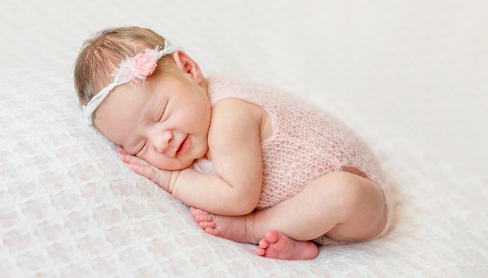 A newborn baby girl in a pink crochet onesie and headband.