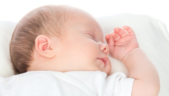 A newborn baby girl sleeping on her back with one arm near her head.