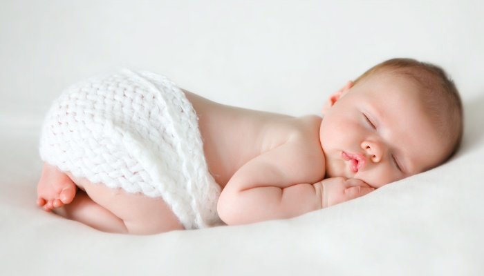 Newborn baby boy sleeping in fetal position with a white crochet blanket.