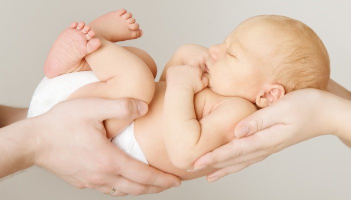A newborn baby being held aloft by his parents' hands.
