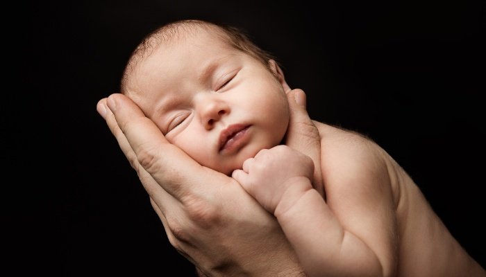 A father holding his new baby in his hands against a black background.