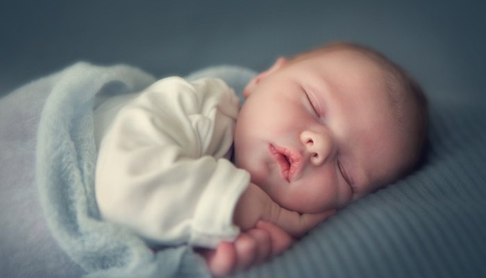 A newborn baby asleep under a light blue fuzzy blanket.