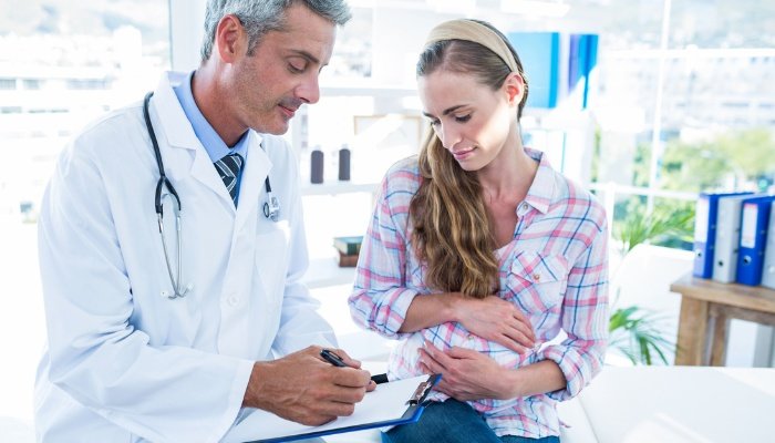A pregnant woman sitting in an examining room consulting with her doctor.