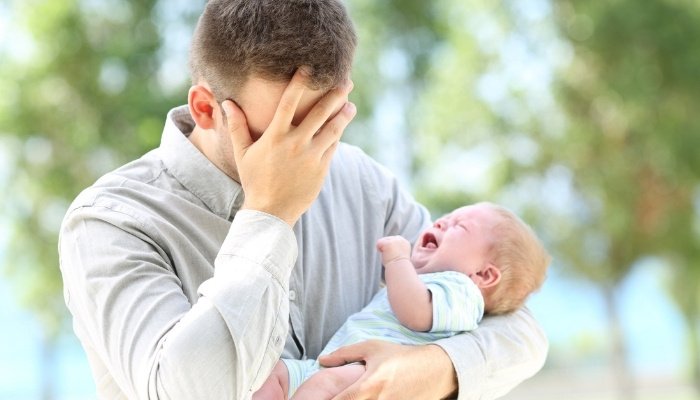 A worried father holding his crying baby outside.