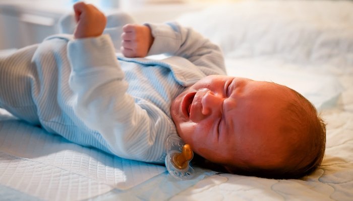 A baby lying on his back crying because of a dropped pacifier.