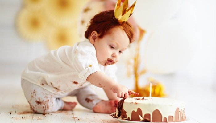 A baby celebrating her first birthday reaching for her birthday cake.