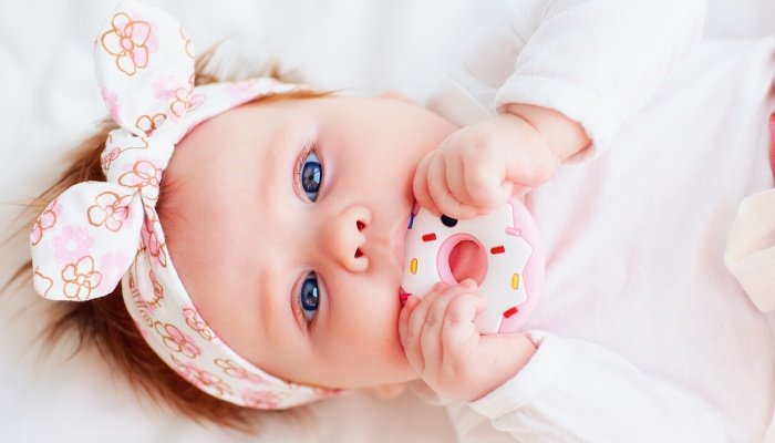 A baby girl lying in her crib chewing on a silicone donut teether.