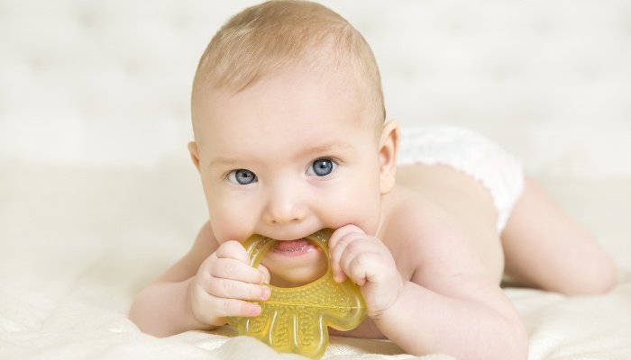 A blue-eyed baby on his tummy chewing on a yellow teether.