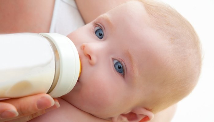 Close look at a cute, blue-eyed baby drinking milk from a bottle.