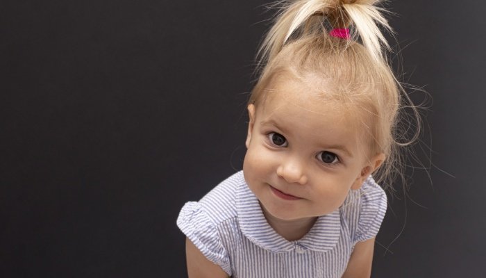 A cute little girl with a high ponytail and an expectant expression on her face.