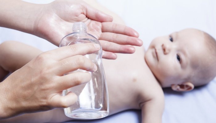 A mother pouring baby oil into her hand to use on her baby.