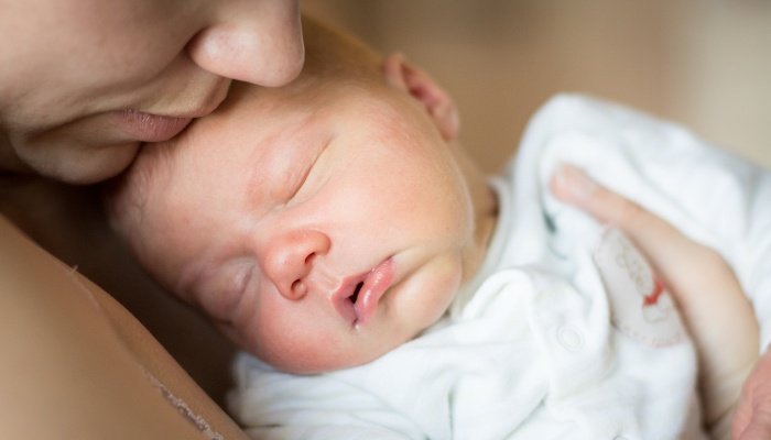 A young mother snuggles her newborn boy close to chest.