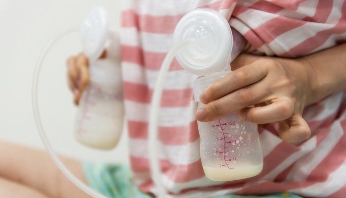 A woman using a breast pump while wearing a striped nursing shirt.