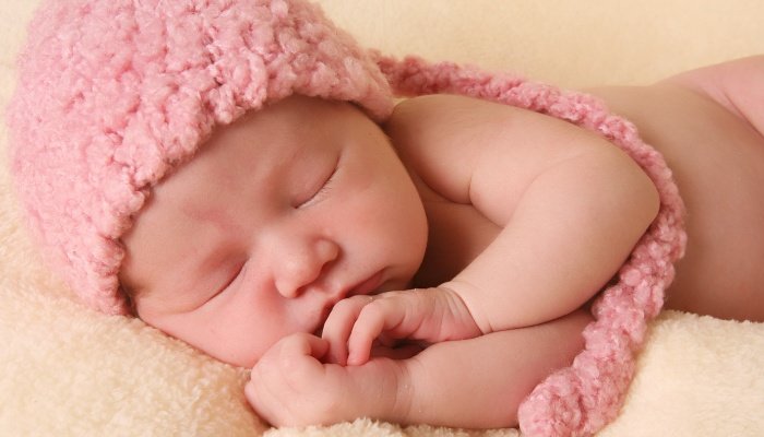 A newborn baby girl lying on her side wearing a pink knit hat.