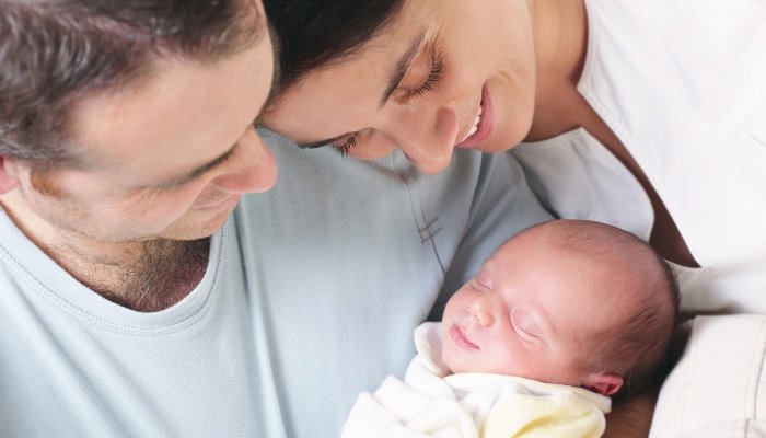 New parents holding their new baby and smiling.
