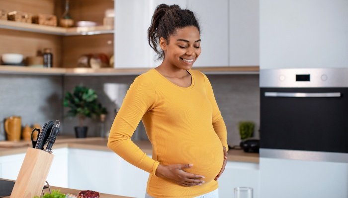 A young pregnant lady standing in her kitchen feeling her baby move.