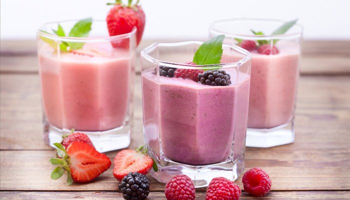 Three berry smoothies with loose berries lying on the table.