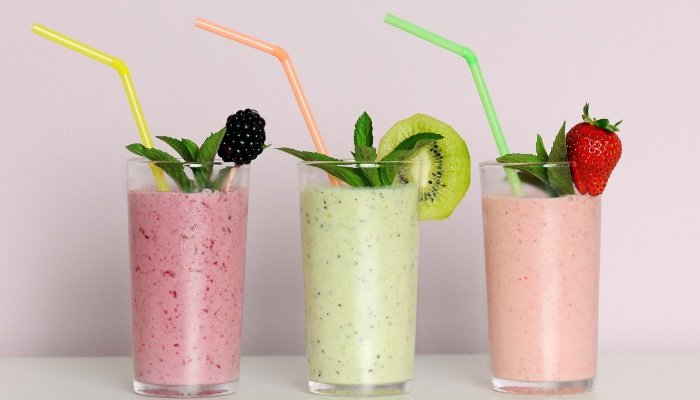 Three different fruit smoothies, each with a colorful straw.