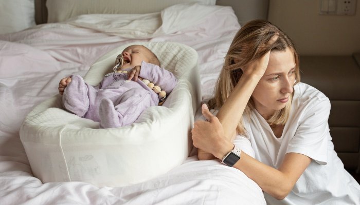 A sad mother sitting beside the bed while her baby cries.