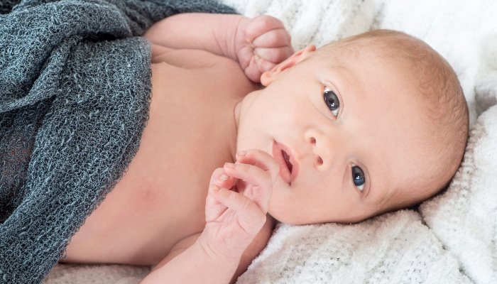 A baby lying in bed with a gray blanket while awake.