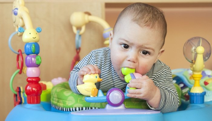 A little boy in a baby bouncer chewing on one of the attached toys.
