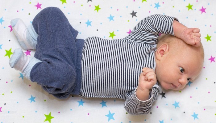 A cute little baby lying in his crib on sheets covered with colorful stars.