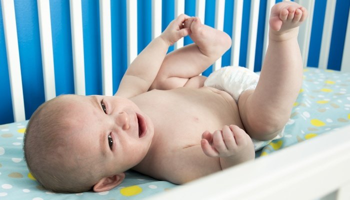 A cute baby happily lying in his crib and playing with his foot.