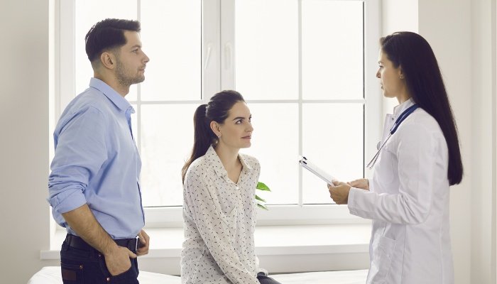 A young couple speaking to a female doctor by a sunny window.