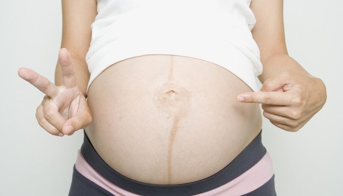 A lady pointing to her pregnant belly with one hand and holding up two fingers with her other hand.