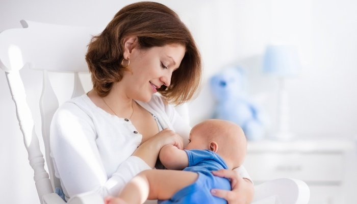 A young mother nursing her baby boy while sitting in a chair.