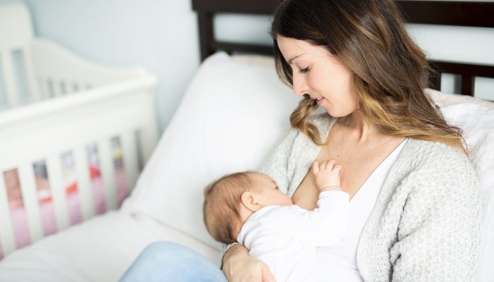 A young mother sitting in her bed breastfeeding her baby.
