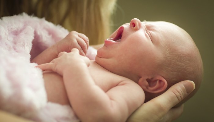 A newborn baby girl yawning while being held in mother's arms.