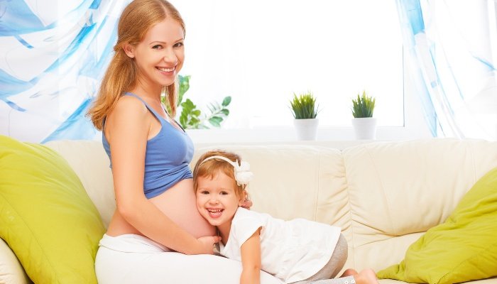 A little girl resting her head on her mother's pregnant belly.