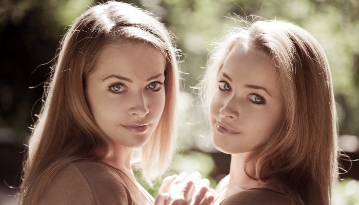 Teenage twin sisters standing front to front outdoors in the sun.
