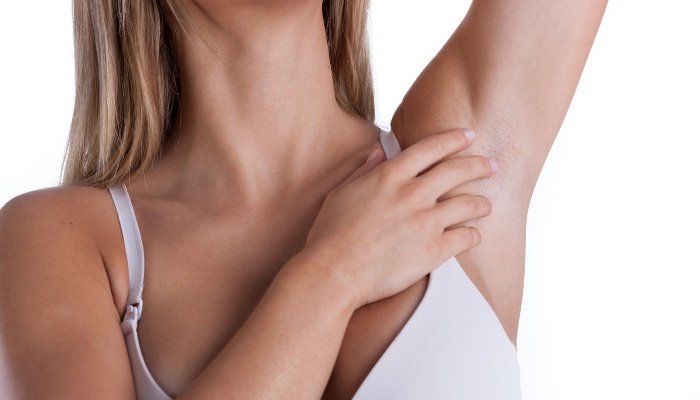 A woman in her bra with her arm raised and fingers touching her armpit.