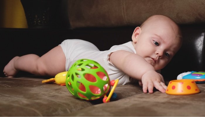 A six-month-old baby lying on her tummy while playing with toys.