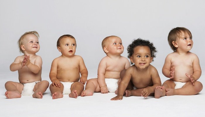 A group of cute babies in diapers sitting in a row against a gray background.