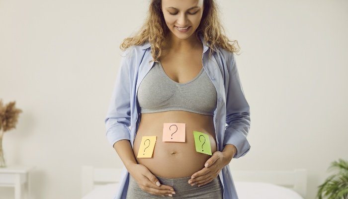 A pregnant lady with question mark sticky notes on her baby bump.