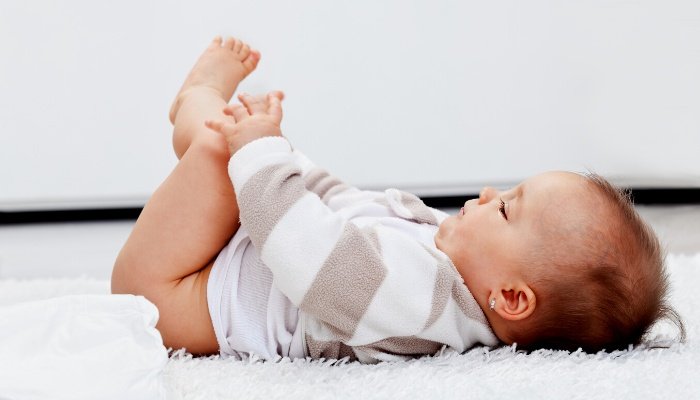 A baby on a changing pad on the floor in the middle of a diaper change.