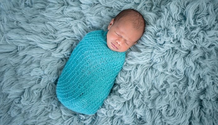 A baby boy tightly swaddled sleeping on a fuzzy blue blanket.