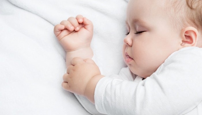 A cute baby fast asleep in white pajamas lying on his side.
