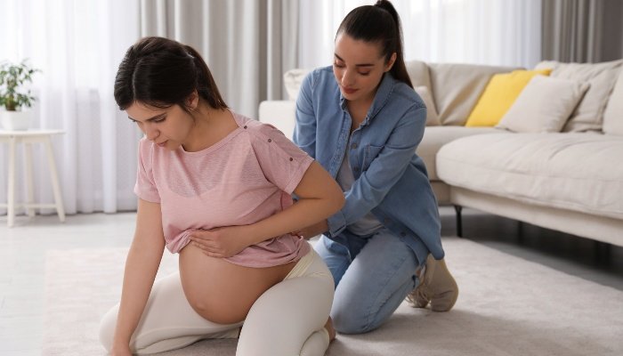 A doula kneeling on the floor behind a pregnant woman to help with comfort levels.