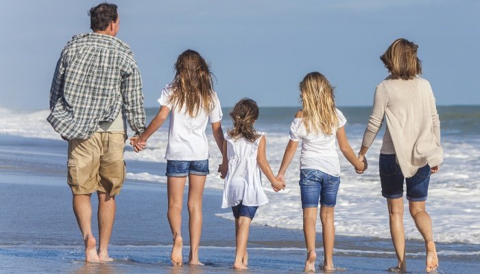 A family walking on the beach while all holding hands.