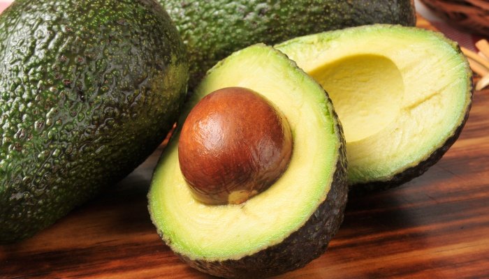 Two whole avocados and one sliced in half to reveal the pit.