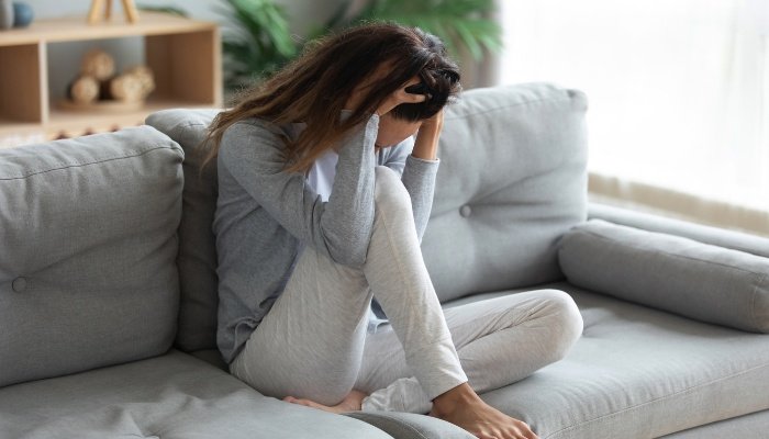A woman sitting on her couch holding her head in her hands as if in pain or dizzy.