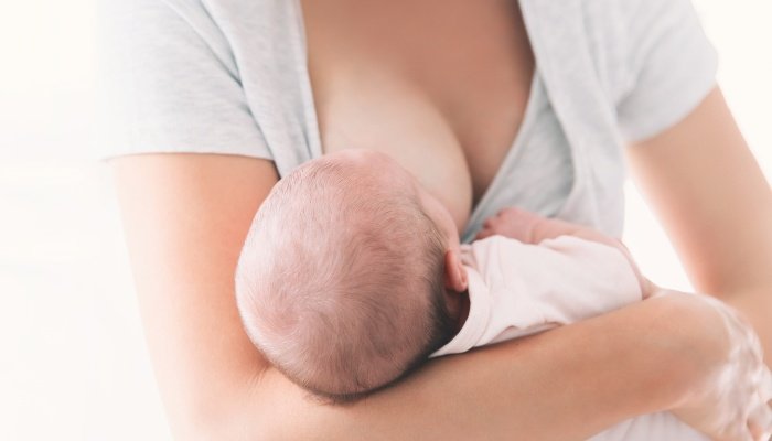 A mother wearing a white shirt breastfeeds her newborn baby.