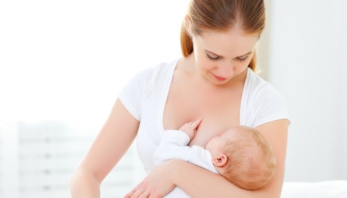 A mother in a white shirt breastfeeding her baby against a white background.