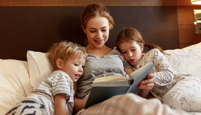 A mother reading a book to her two young children in bed.
