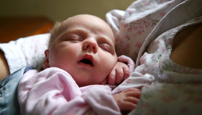 A newborn baby girl fast asleep in her mother's arms.